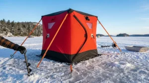 A photorealistic 4K detailed view of the red and black portable ice fishing hut, featuring the primary 'CANADIAN FISHING GEAR / ÉQUIPEMENT DE PÊCHE CANADIEN' bilingual branding and detailed white safety instruction panels in both English and French, including graphic icons with text pointers, during the early morning on a frozen lake.
