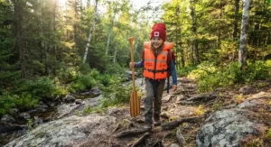 A young camper wearing their lightweight kids PFD for canoe camping while hiking a scenic Canadian Shield portage trail.