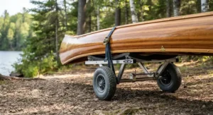 An adjustable folding canoe cart securely strapped underneath the wide hull of a touring canoe
