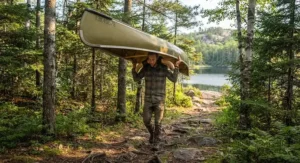 A Canadian canoeist carrying a solo canoe overhead using a contoured portage yoke on a forest trail.