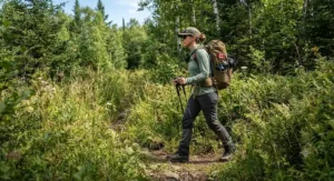 Hiker walking through tall brush on a trail, protected by permethrin clothing spray applied to their hiking clothes.